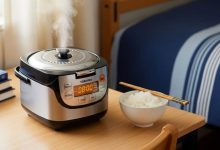 Compact Toshiba mini rice cooker on a wooden dorm desk with steam rising