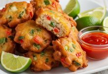 Golden crispy Jamaican saltfish fritters on white plate with lime wedges and hot pepper sauce for dipping