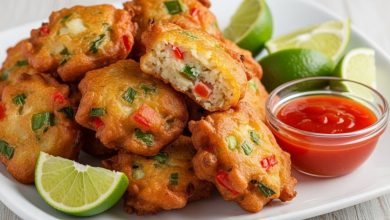 Golden crispy Jamaican saltfish fritters on white plate with lime wedges and hot pepper sauce for dipping