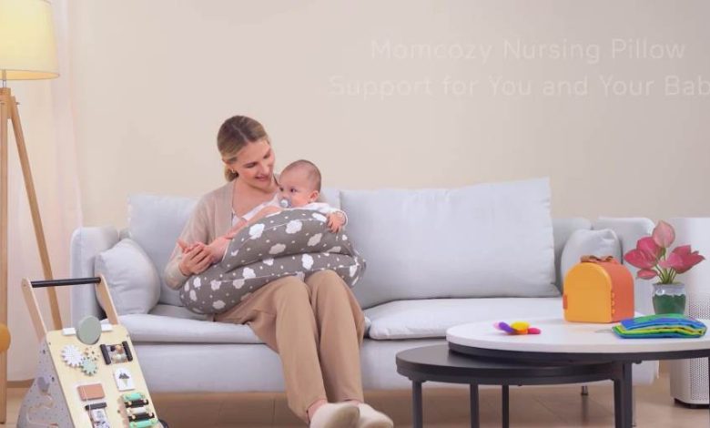Mom smiling while breastfeeding newborn on Momcozy nursing pillow in cozy nursery