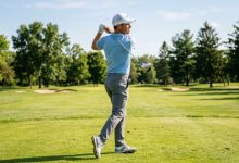 A golfer wearing a white breathable mesh-back golf cap while standing on a sunny fairway mid-swing