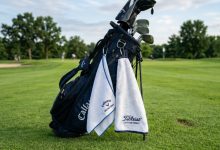 Side-by-side comparison of a microfiber golf towel and a cotton terry golf towel clipped to a golf bag on a green fairway