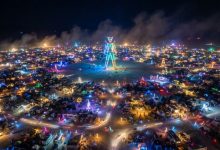 Aerial view of Black Rock City at night during Burning Man 2026 with the Man structure lit at the center