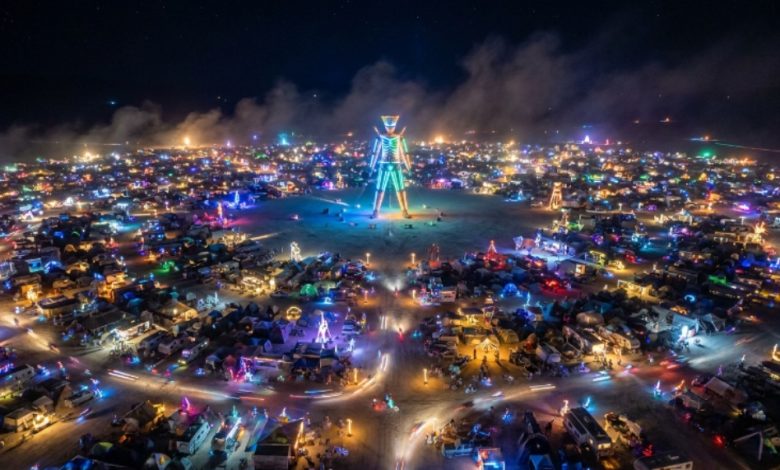 Aerial view of Black Rock City at night during Burning Man 2026 with the Man structure lit at the center