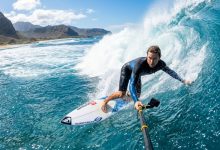 Surfer holding a waterproof camera while riding an ocean wave.